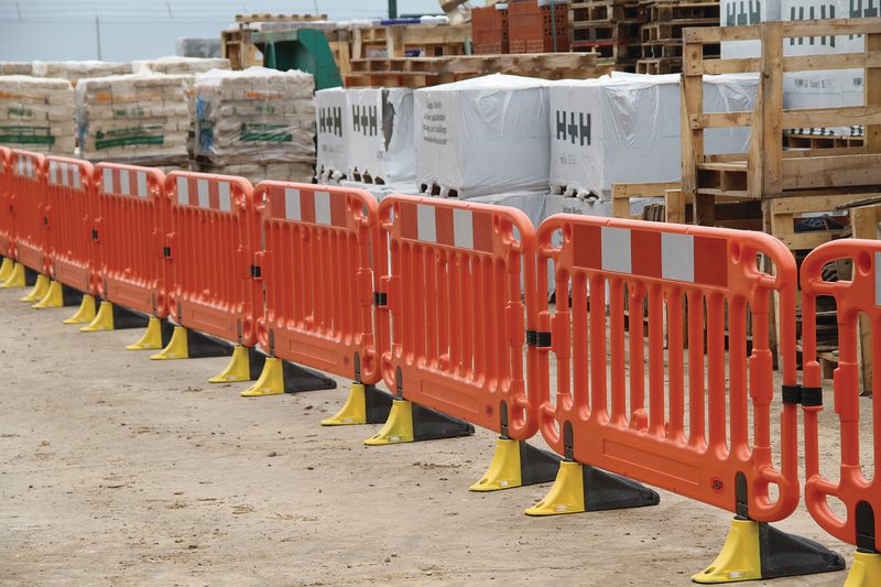 Work site with pedestrian barrier fences all attached in a row. They are orange in colour with hi-vis panels across the top for visibility and yellow and grey feet. 